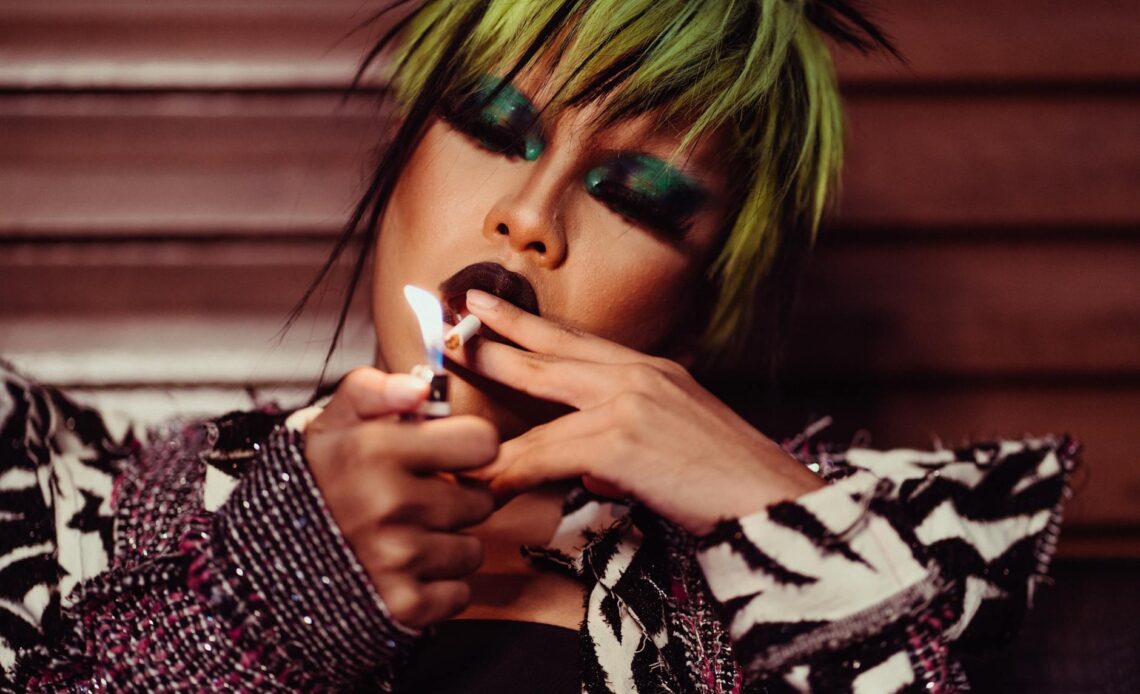 crop expressive transgender lighting cigarette with closed eyes