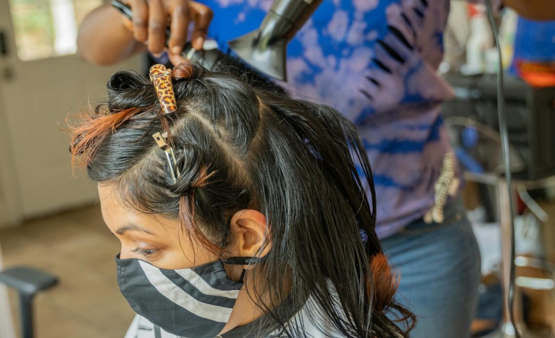 a person wearing face mask having her hair blow dry