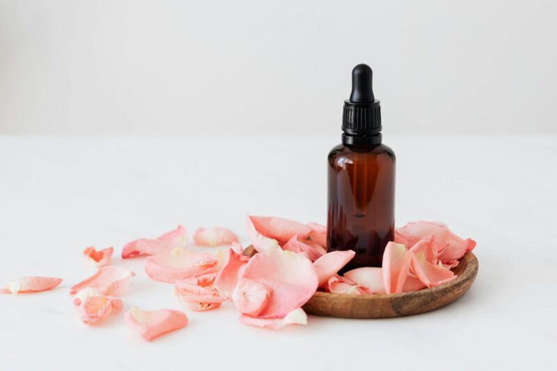 essence bottle put on wooden plate near rose petals