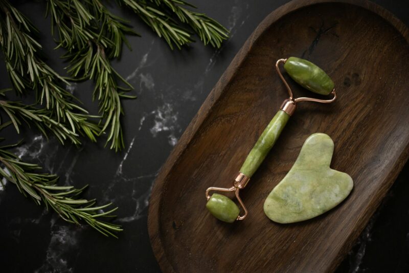 facial massager with gua sha on timber tray near rosemary