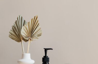 set of cosmetic supplies near decorative leaves in vase on marble shelf