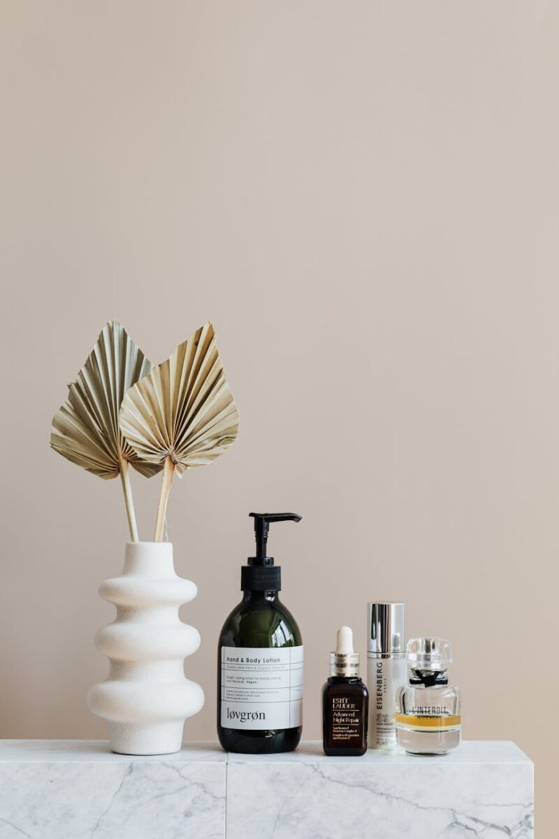 set of cosmetic supplies near decorative leaves in vase on marble shelf