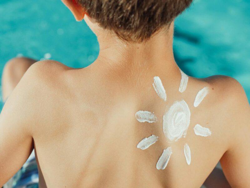 sun drawing sunscreen on child s back photo